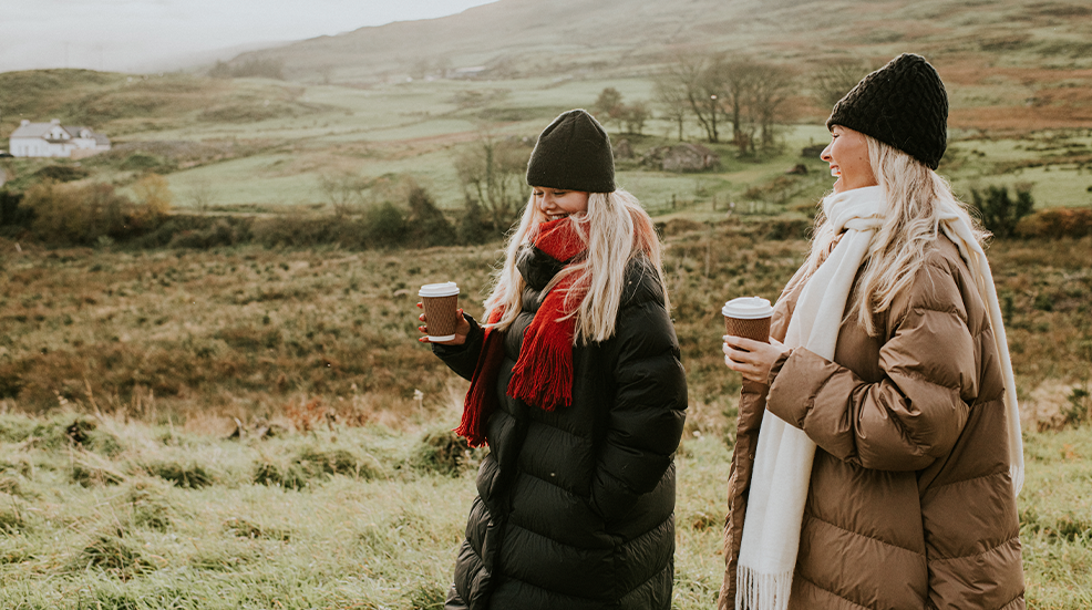 Two, young, beautiful woman enjoy a walk outdoors, dressed in warm clothing, clutching takeaway coffee cups
